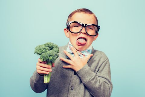 Kleiner Junge mit Brille ekelt sich vor einem Brokkoli, den er in der Hand hält