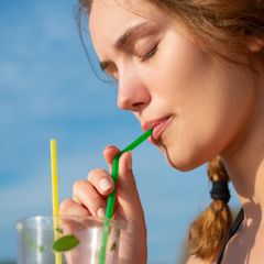 Eine junge Frau trinkt aus einem Plastikstrohhalm