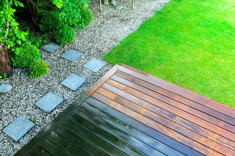 Teilweise gereinigte Holzterrasse mit Druckreiniger durch den grünen Rasen