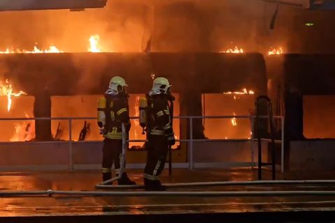 Zwei Feuerwehrleute stehen auf dem Bahnsteig in Berlin-Ahrensfelde und löschen einen brennenden Zug