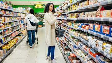 A woman reading an item label and browsing products while grocery shopping in her local supermarket.