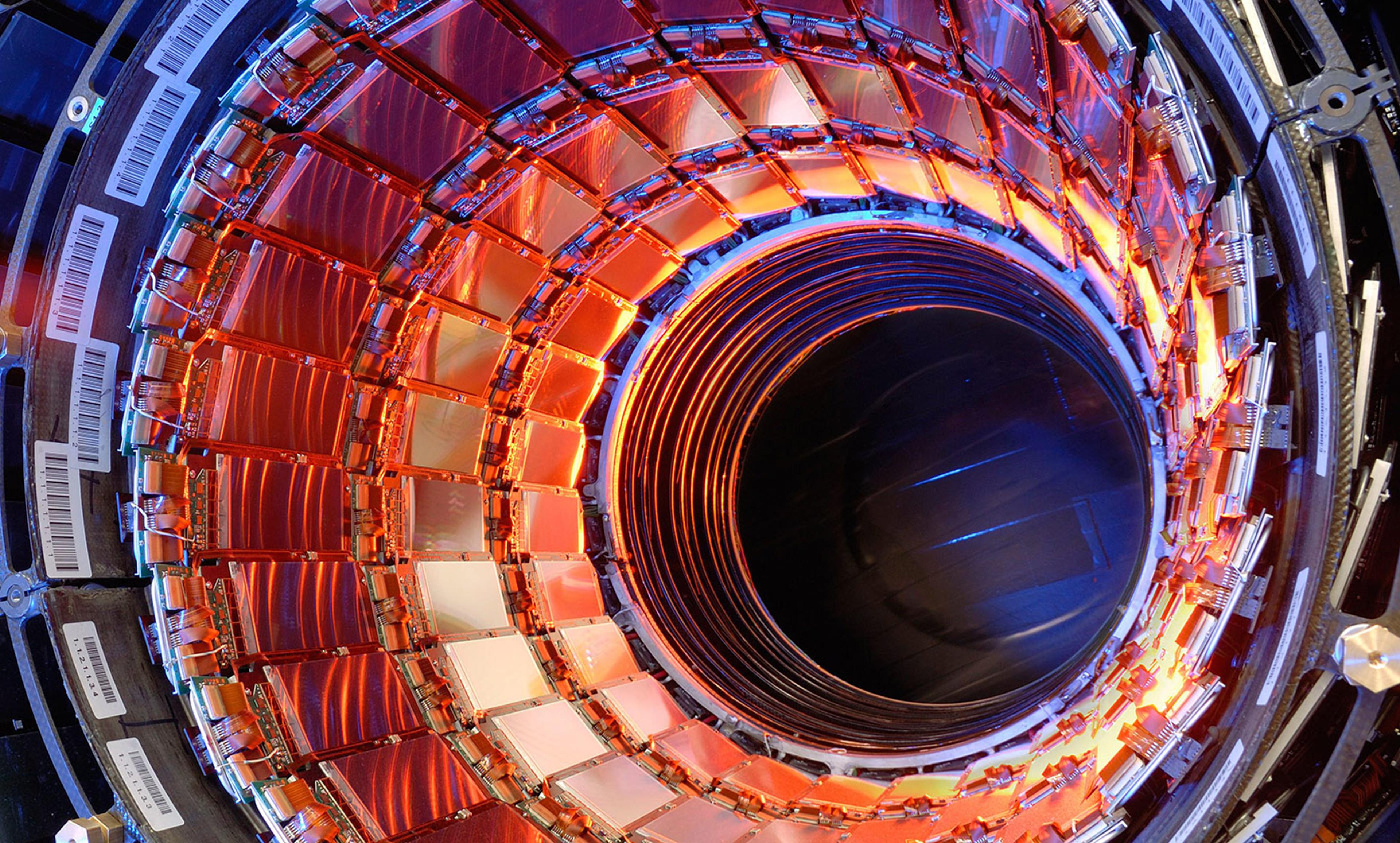 A brightly lit circular structure with red, orange and blue elements, resembling part of a scientific or industrial machine.