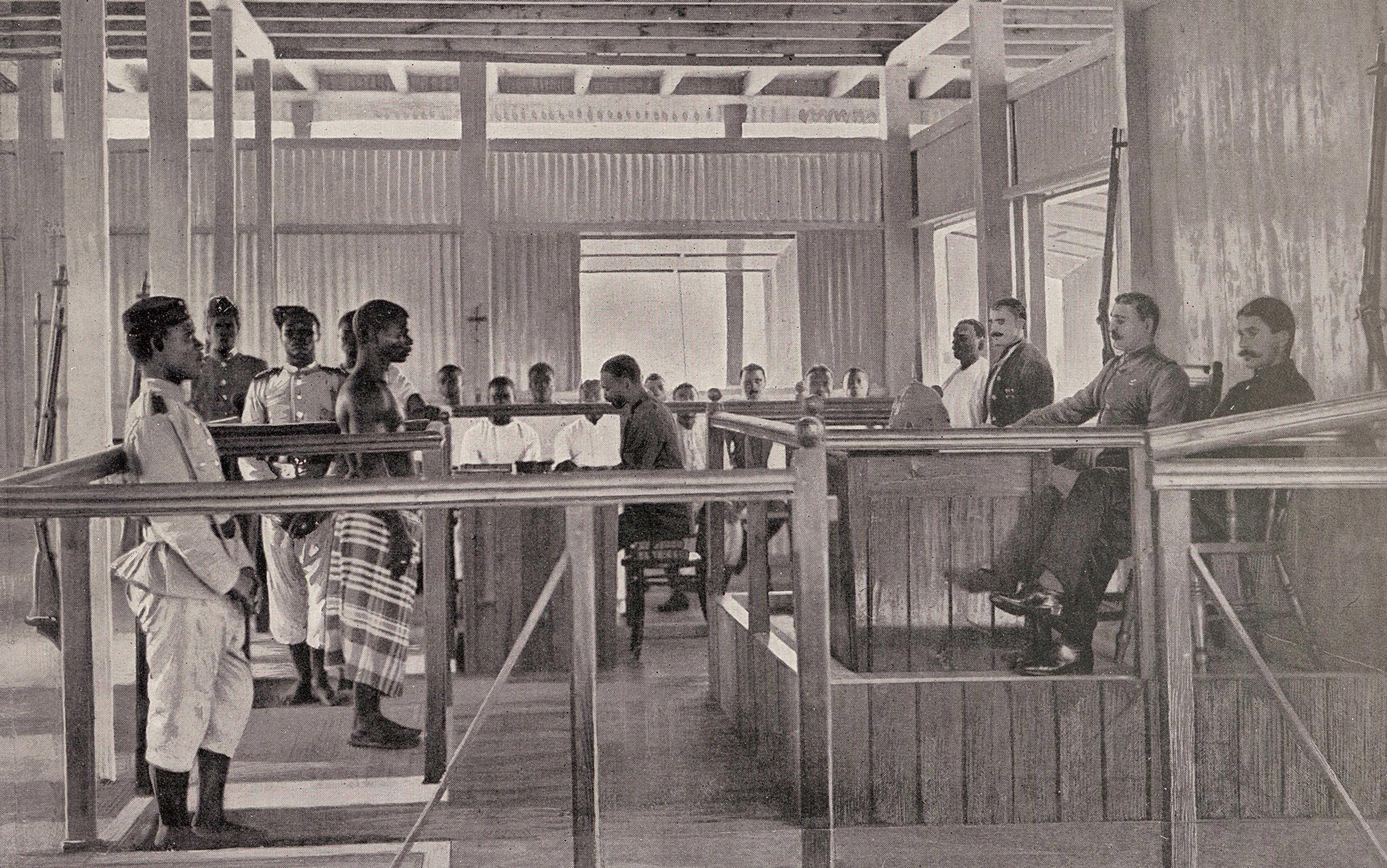 Vintage black-and-white photo of a colonial-era courtroom with seated officials and standing West African defendants in traditional attire.