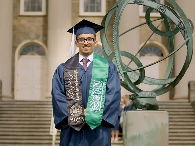 Photo of student in graduation gown standing in front of Old Main steps