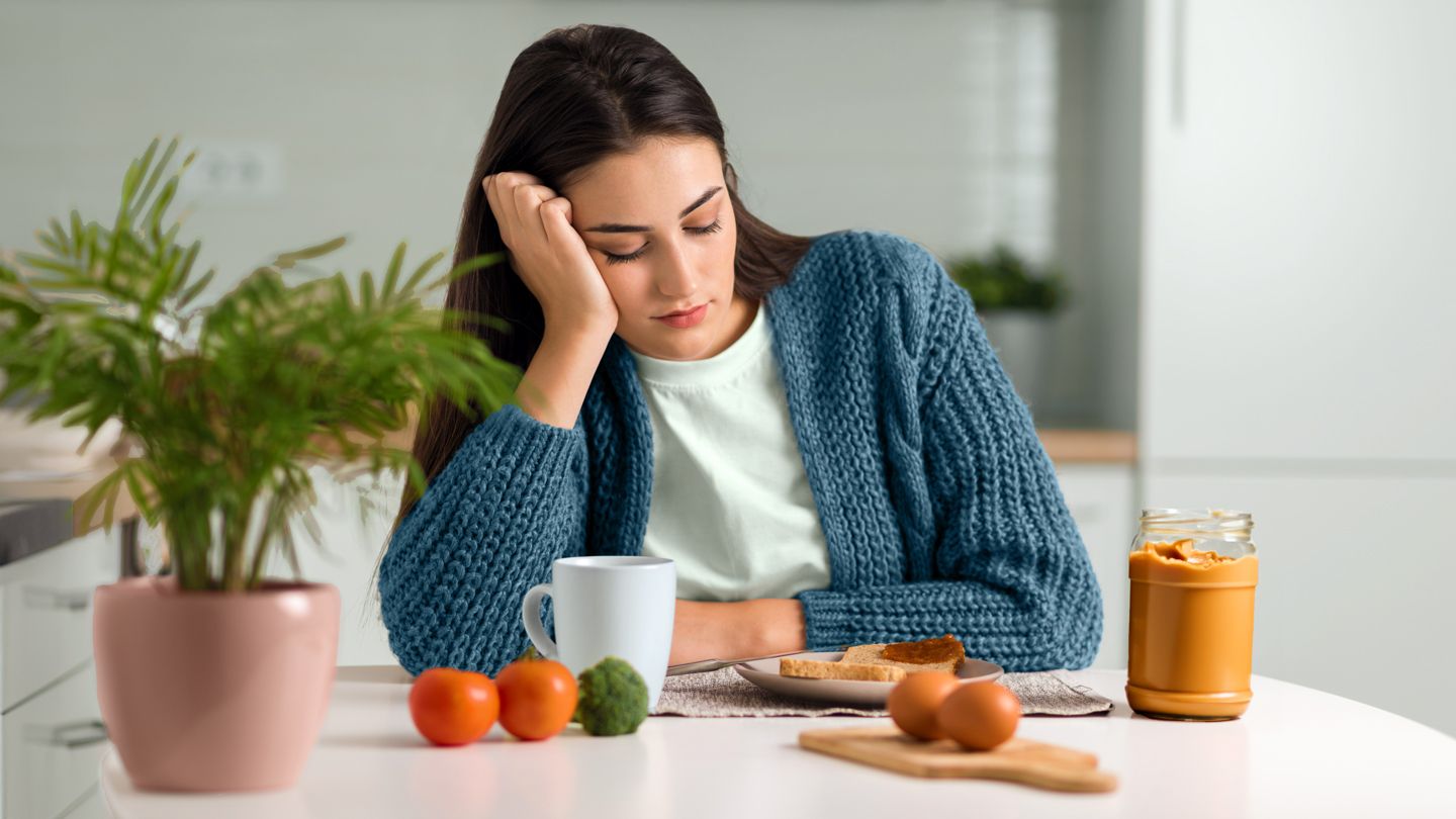 young woman looking unhappily at food on her kitchen table