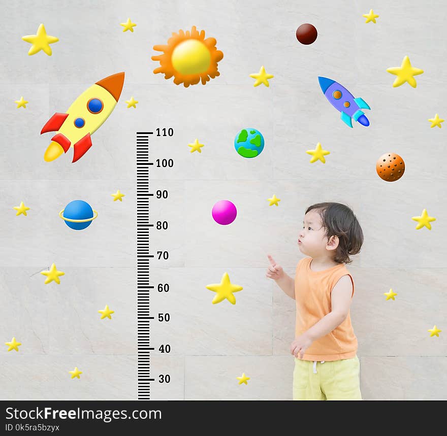 Closeup happy asian kid stand and point to scale of measure height with cute cartoon at the marble stone wall textured background