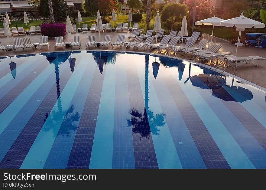 Beautiful reflection in clear water of blue swimming pool with chaise-longues in luxury resort hotel