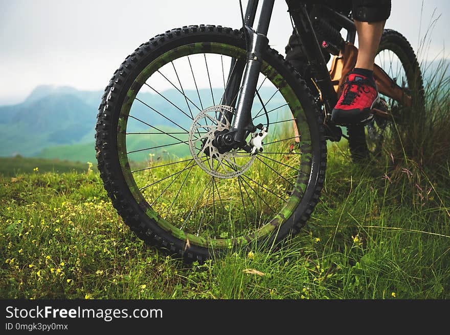 Close-up of a mountain bike wheel in the mountains on the green grass and foot of a rider