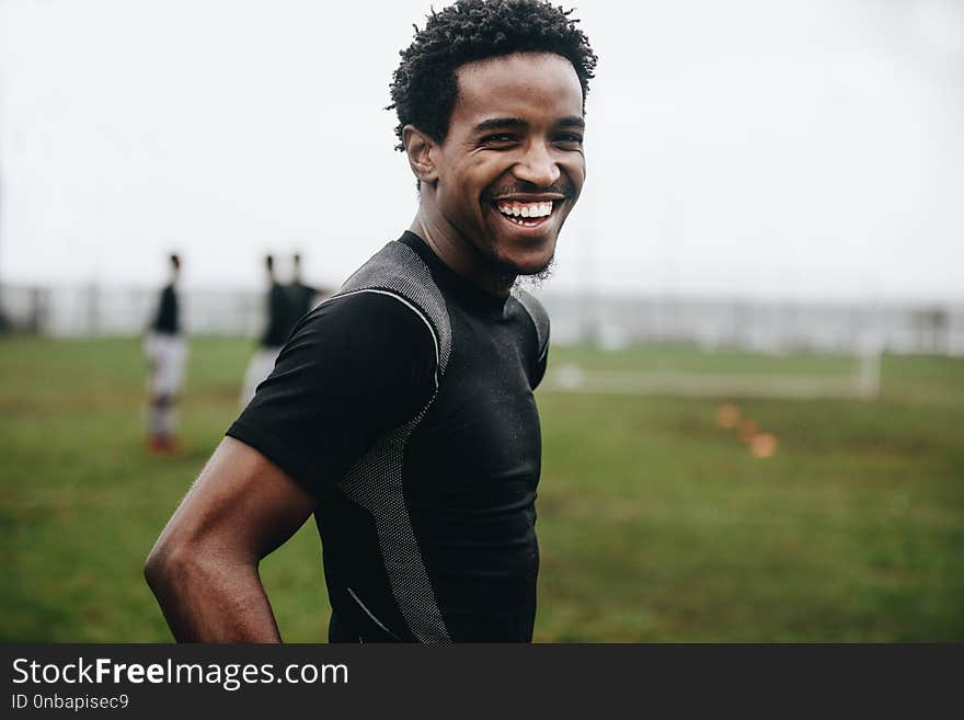 Portrait of a cheerful footballer standing on field during practice. Side view of an african soccer player standing on football