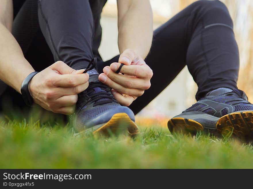 A young man in black clothes is tying the laces on the sneakers close up. fitness athlete sitting on the sports field on the grass