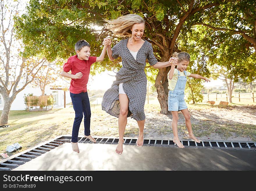 Mother Playing With Children On Outdoor Trampoline In Garden