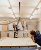 After using a digitally controlled milling machine to slice through fiberboard, Caradec using an air hose to clean out the wood dust between each pass of the mill.