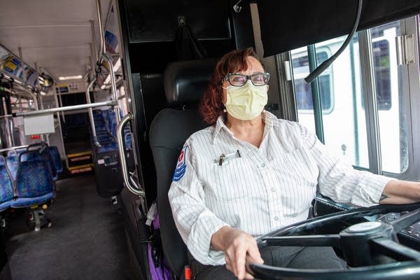 A woman sits at the driver seat of a bus.