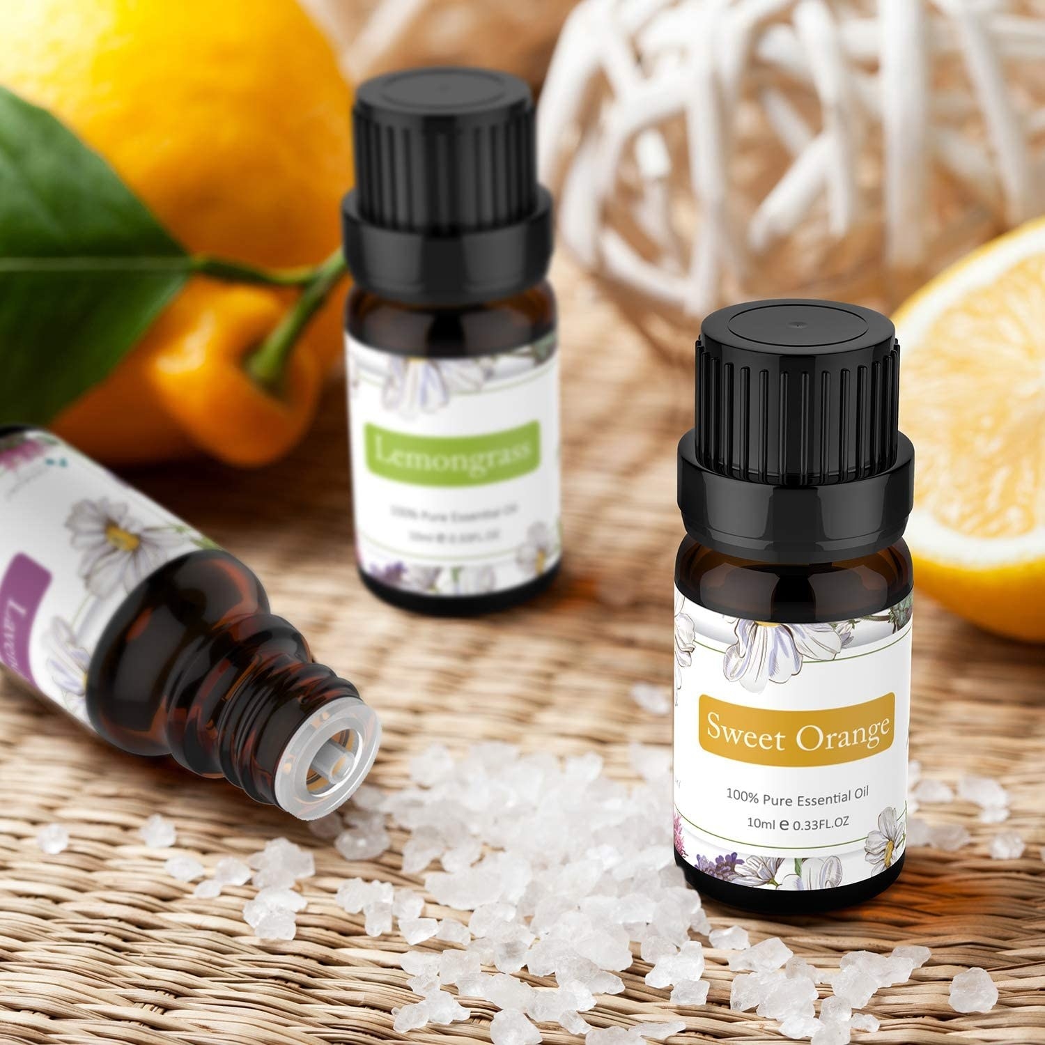 Three essential oil bottles labeled as Sweet Orange, Lemongrass, and a third partially visible. Surrounding them are lemon slices and coarse salt