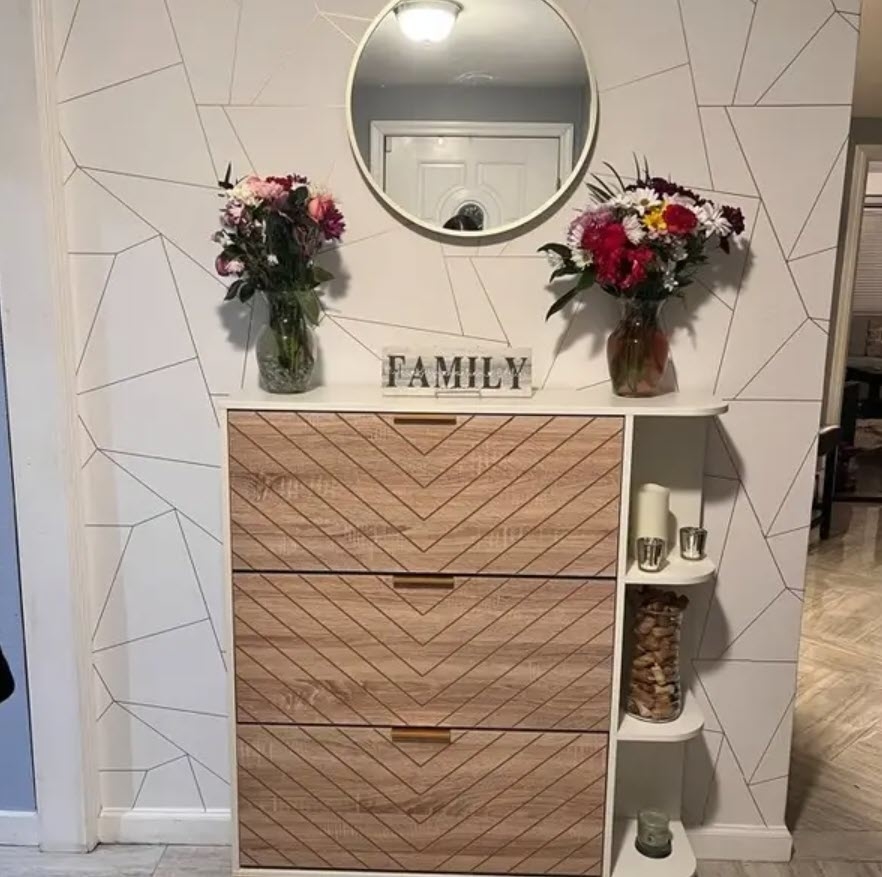 A wooden dresser with three drawers and a circular mirror above it. Two flower vases and a &quot;FAMILY&quot; sign are on top, with a small shelf on the side holding various items