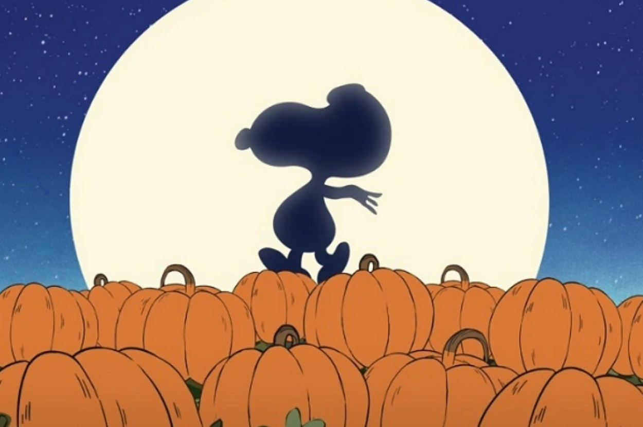 Snoopy's silhouette is shown dancing on top of pumpkins in front of a large moon