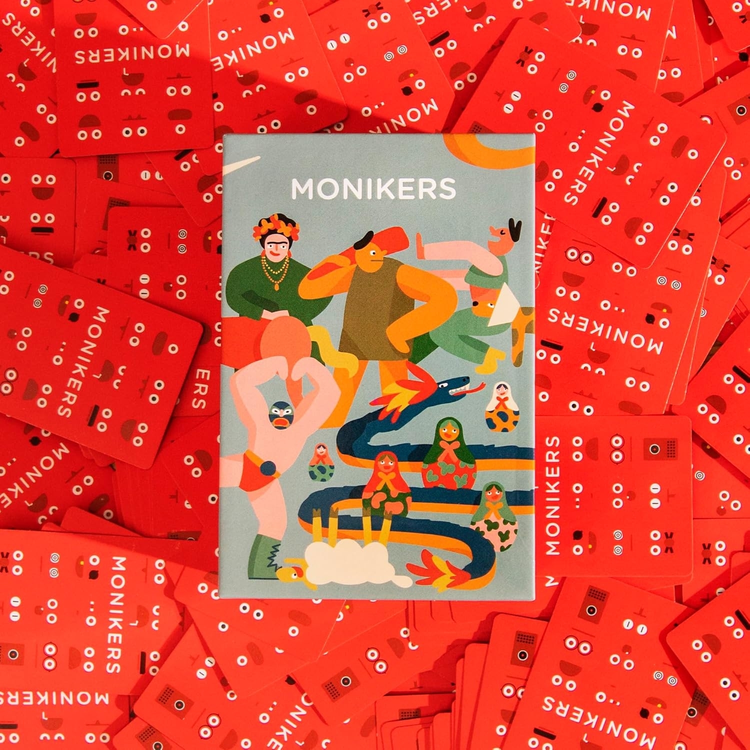 A variety of colorful Monikers game cards are scattered, featuring playful illustrations. This image highlights the shopping category for Monikers card game