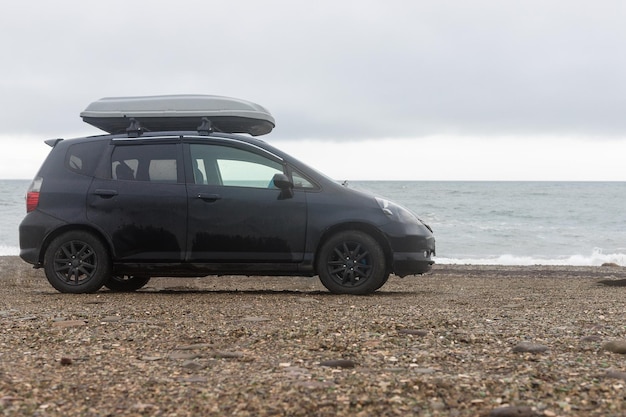 A black car on the beach in summercar parking on the sea beach\
with a trunkcar roof with luggage box on rooftop on the rack\
systemsummer trip or auto travel adventure conceptcopy space