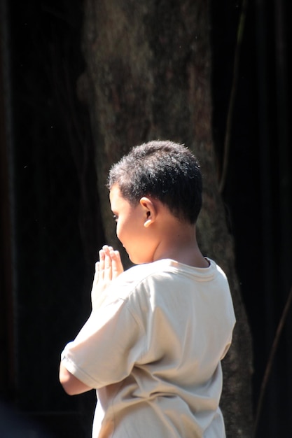 Premium Photo | Boy with hands clasped standing against tree trunk