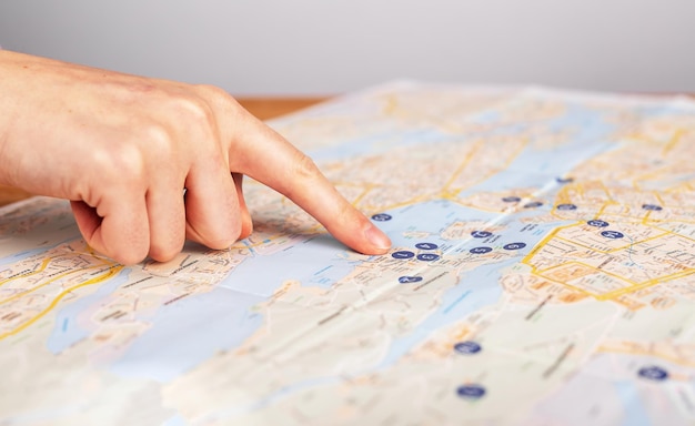 Finger pointing on location on paper map closeup abstract\
travel route concept