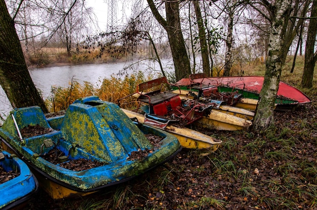 Old boats and catamarans are rusting in the open dump in the\
forest at the foot of the river bank of outdated water equipment\
nearby grow large birches and other trees environmental\
pollution