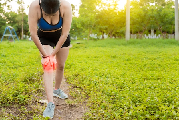 Runner woman with knee pain outdoors athlete knee pain and\
fractures concept athlete woman with knee muscle pain athlete girl\
on the ground with knee pain outdoors