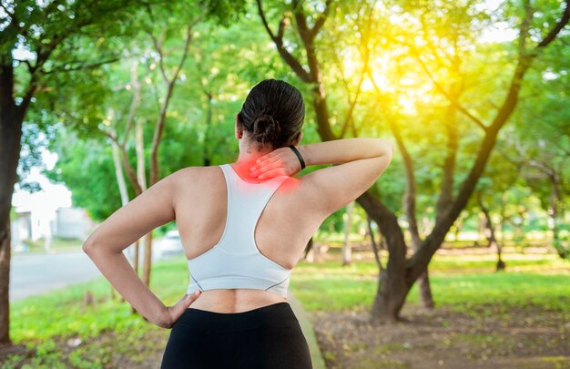 Running woman with shoulder muscle pain in a park shoulder pain\
concept of a runner athlete athlete girl in pain rubbing her\
shoulder outdoors back view of sporty woman with shoulder pain