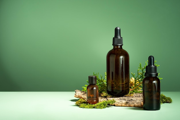 A set of brown glass bottles moss and tree bark on a green\
background oil with serum for skin and hair care glass bottle of\
essential body oil with a dropper selfcare and wellness copy\
space