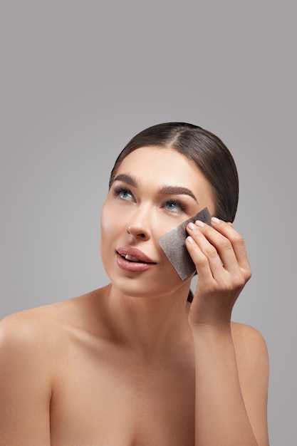 Skin care. young woman removing oil from face using blotting\
papers. beautiful girl model with smooth and healthy skin.