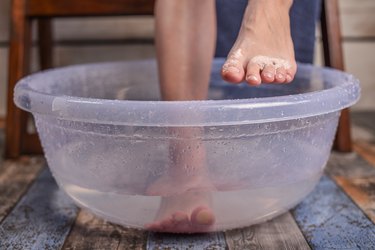 a person's feet soaking in a bowl of water, as an example of ingrown toenail self-care