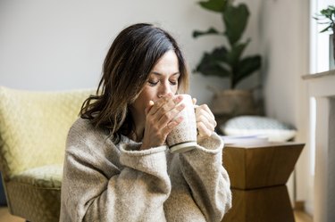 A person with long brown hair at home drinking tea as a natural remedy for a sore throat