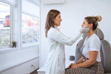 A person wearing a white shirt and ponytail sitting at the dermatologist's office, getting an exam