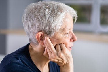 an older adult with short white hair touching their plugged ear while resting during a workout