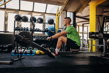 young adult wearing a green T-shirt and black shorts getting rowing machine benefits at the gym