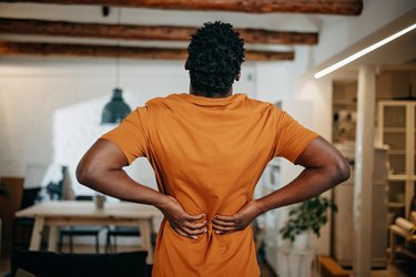 Back view of a young black person in an orange shirt clutching back in pain