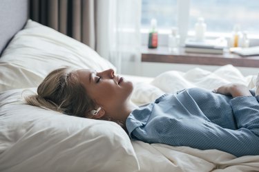 A Beautiful Woman Listening to Music While Lying On The Bed In Her Blue Pajamas, as a tinnitus remedy