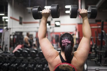 Rear view of a woman wearing a sports bra exercising with dumbbells  at the gym.