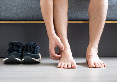 Close up of a barefoot person reaching down to scratch their itchy ankles