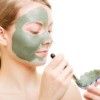 Woman applying green facial mask with a brush.