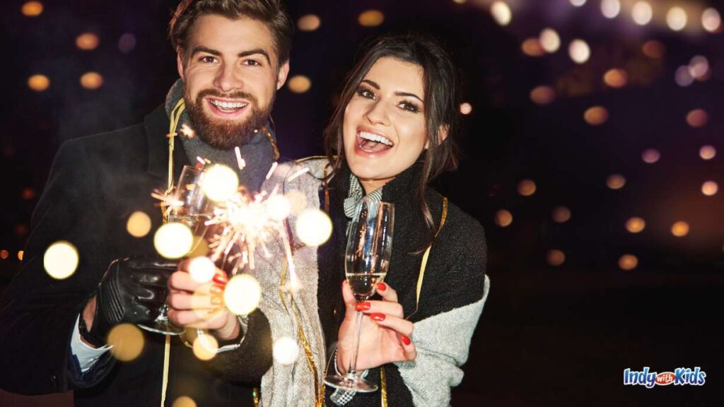 Things to Do in Indianapolis New Year’s Eve: a couple hold champagne glasses and sparklers outside at night