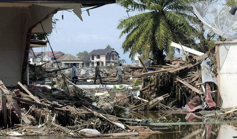 BANDA ACEH, INDONESIA: Passersby walk amid debris of destroyed buildings, 27 December 2004 in Banda Aceh, after tidal waves hit the region. The carnage suffered when Indonesia was hit at point-blank range by a giant earthquake and tidal wave began to emerge Monday as links were restored to remote areas and the death toll rose to at least 4,725. Surging oceans and seismic shockwaves wreaked havoc across Asia, and struck particularly hard in the conflict-battered and impoverished Indonesian province of Aceh where they unleashed a brutal force of death and destruction. AFP PHOTO/BAY ISMOYO (Photo credit should read BAY ISMOYO/AFP via Getty Images)