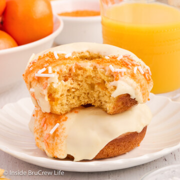 Two donuts with a bite out of the top one on a white plate.