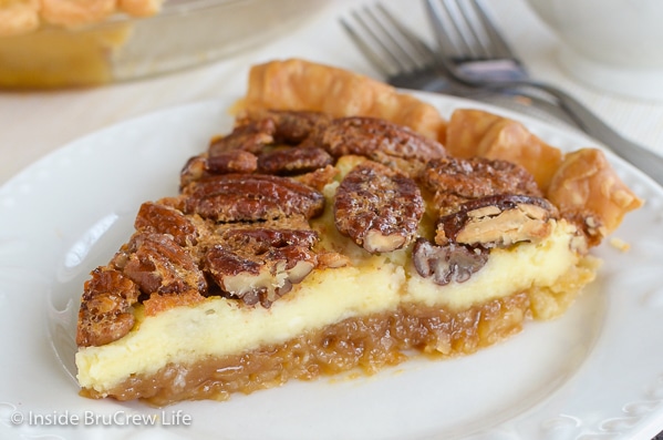 A slice of pecan cheesecake pie on a white plate with two forks behind it.