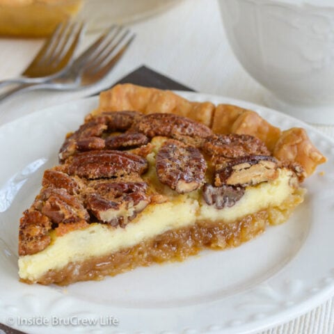 A white plate with a slice of pecan pie cheesecake on it.