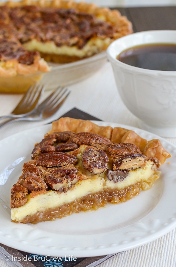 A slice of pecan cheesecake pie on a white plate with the whole pie behind it.