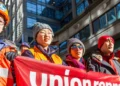 a group of diverse workers standing together, united under a banner bearing the words