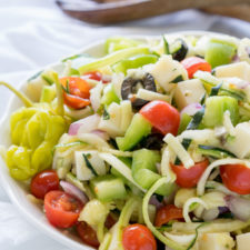 A close up of a bowl of salad, with zucchini noodles, tomatoes, olives, and other veggies