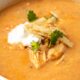 creamy chicken enchilada soup in white bowl with sour cream and tortilla strips on top.