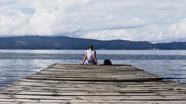 Person Sitting on Brown Wooden Dock Under Cloudy Blue Sky