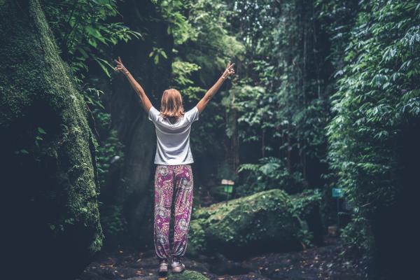 Woman With Raising Arms Facing Pathway Between Forest Trees